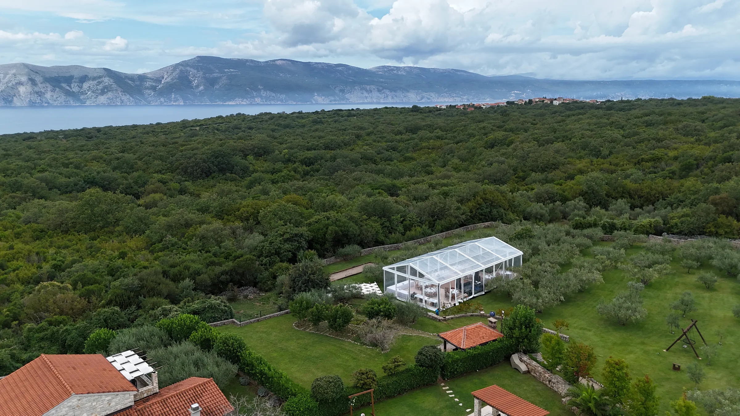 Pogled dronom na prozirni šator u masliniku s pogledom na more